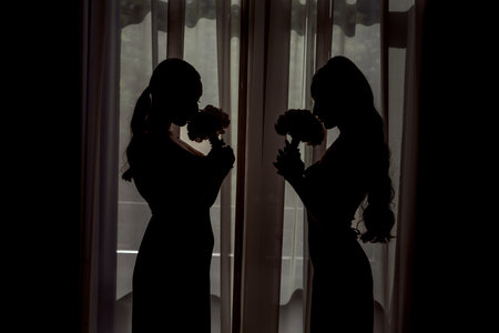 Silhouette of the bride and groom standing near the window at homeの写真素材