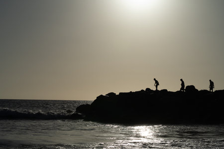 Silhouette of people on the rocks in the sea at sunsetの写真素材