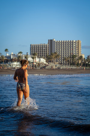 Beautiful young woman in bikini standing on the black sand beach Troya at sunset Tenerife Spain.の写真素材