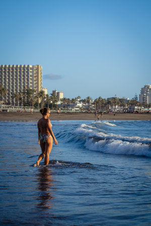 Beautiful young woman in bikini standing on the black sand beach at sunset.の写真素材