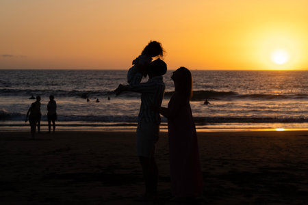 Silhouette of mother and daughter and father on the beach at sunset.の写真素材