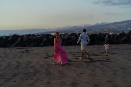 Young family of three having fun on the  on the black sand beach Troya at sunset Tenerife Spain.の写真素材