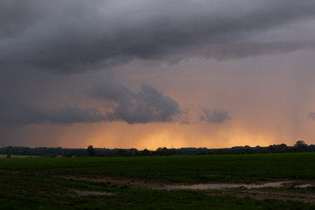 Dramatic sky with stormy clouds over green field at sunsetの写真素材