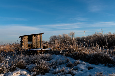 Winter landscape with old wooden hut in the field covered with frost.の写真素材