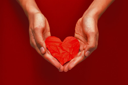 Beautiful female hand holding the crumpled red paper heartの写真素材