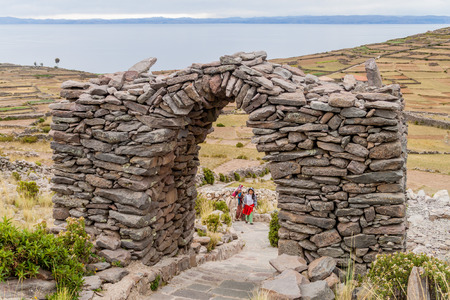 AMANTANI, PERU - MAY 15, 2015: Locals go on a path through a stone arch on Pachatata hill on Amantani island in Titicaca lake, Peruの写真素材