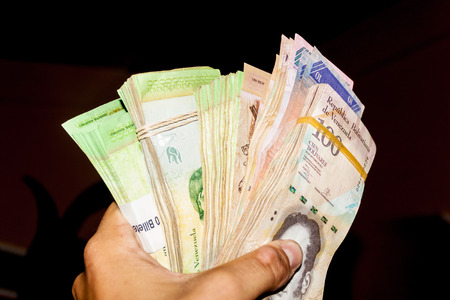 Stack of Venezuelan currency (Bolivar Fuerte) is hold in the hand. Due to hyperinflation, it is...