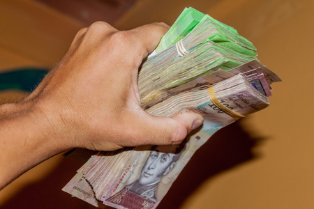 Stack of Venezuelan currency (Bolivar Fuerte) is hold in the hand. Due to hyperinflation, it is necessary to use thick stack of bills to cover basic needs.の写真素材