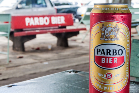 PARAMARIBO, SURINAME - AUGUST 6, 2015: Can of Parbo beer, product of Surinamese Brewery,  subsidiary of Heineken. Parbo advertisement on a bench, out of focus.のeditorial素材