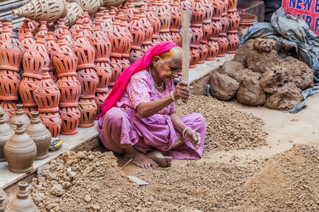 DELHI, INDIA - OCTOBER 22, 2016: Old woman crushing pieces of clay in the center of Delhi, India.のeditorial素材