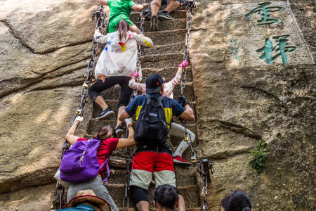 HUA SHAN, CHINA - AUGUST 4, 2018: People climbing steep stairs leading to the peaks of Hua Shan...
