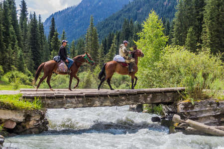 KARAKOL, KYRGYZSTAN - JULY 16, 2018: Local horse riders are crossing a bridge over Karakol river in Kyrgyzstanのeditorial素材