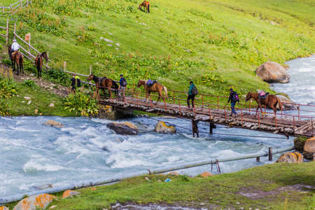 ALTYN ARASHAN, KYRGYZSTAN - JULY 18, 2018: Horsemen cross a foot bridge over Arashan river in Altyn Arashan village, Kyrgyzstanのeditorial素材