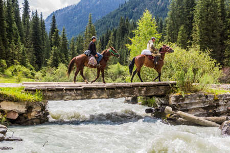 KARAKOL, KYRGYZSTAN - JULY 16, 2018: Local horse riders are crossing a bridge over Karakol river in Kyrgyzstanのeditorial素材