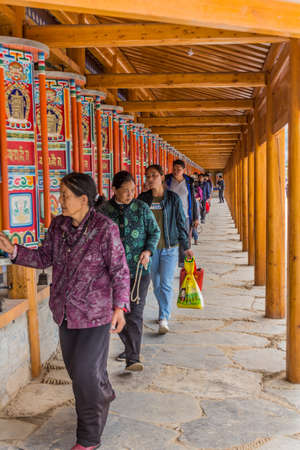 XIAHE, CHINA - AUGUST 25, 2018: Devotees pass a row of praying wheels around Labrang Monastery in Xiahe town, Gansu province, Chinaのeditorial素材