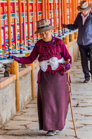 XIAHE, CHINA - AUGUST 25, 2018: Devotees pass a row of praying wheels around Labrang Monastery in...