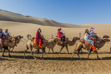 DUNHUANG, CHINA - AUGUST 21, 2018: Tourists ride camels at Singing Sands Dune near Dunhuang, Gansu Province, Chinaのeditorial素材