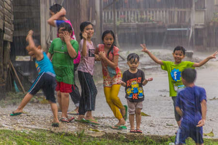 KINABATANGAN, MALAYSIA - FEBRUARY 19, 2018: Children playing in a heavy rain in a small village near Kinabatangan river, Sabah, Malaysiaのeditorial素材