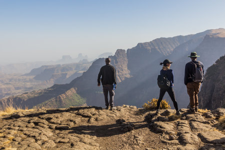 SIMIEN MOUNTAINS, ETHIOPIA - MARCH 16, 2019: Tourists with a local guide looking into the northern...