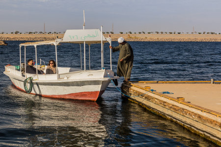 ASWAN, EGYPT - FEB 13, 2019: Boat near Kalabsha temple in the Nasser lake with the Aswan high dam in the background, Egyptのeditorial素材