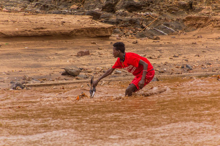 OMO VALLEY, ETHIOPIA - FEBRUARY 4, 2020: Local boy on a motorbike crossing swollen waters of Kizo...