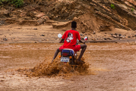 OMO VALLEY, ETHIOPIA - FEBRUARY 4, 2020: Local boy on a motorbike crossing swollen waters of Kizo river, Ethiopiaのeditorial素材