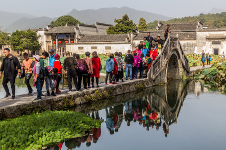 HONGCUN, CHINA - OCTOBER 29, 2019: People cross a bridge over South lake in Hongcun village, Anhui province, Chinaのeditorial素材