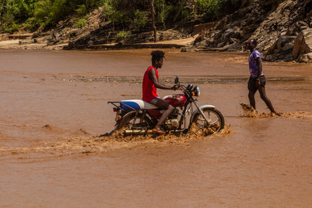 OMO VALLEY, ETHIOPIA - FEBRUARY 4, 2020: Local boy on a motorbike crossing swollen waters of Kizo river, Ethiopiaのeditorial素材
