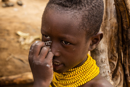 KORCHO, ETHIOPIA - FEBRUARY 4, 2020: Karo tribe boy in his Korcho village getting his face painted,...