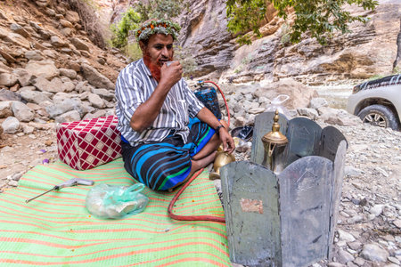 WADI LAJAB, SAUDI ARABIA - NOVEMBER 25, 2021: Local man wearing a traditional floral headpiece making coffee in Wadi Lajab canyon, Saudi Arabiaのeditorial素材