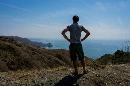 Young man standing and overlooking the bech at pacific ocean inの写真素材
