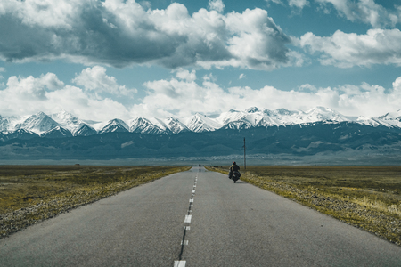 Motor cyclist on Street in steppe with Tian Shan mountains in background, Kazakhstan Central Asiaの写真素材
