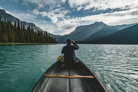 Young Man Canoeing on Emerald Lake in the rocky mountains canada with canoe and mountains in the background blue water.の写真素材