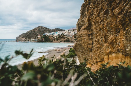 Crete, Greece. View from cliffs to village with marine vessels, boats and lighthouse. View from cliff on Bay with beach and architecture - vacation destination resort with clear ocean water. Rethymno, Crete, Greeceの写真素材