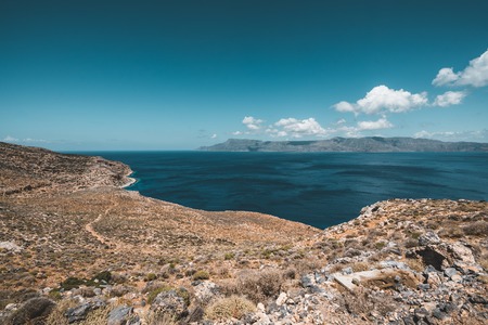 Panoramic view of rocks and beach with sky and clouds in Crete, Greece. Amazing scenery with crystal clear water and the rock formation against a deep blue sky during Summer period. Greece, Europeの写真素材