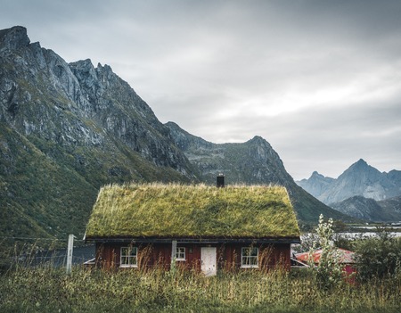 Lofoten Islands Norway - September 2018: House with traditional grass roof and mountains in the background on a cloudy day. Lofoten is an archipelago and a traditional district in the county of Nordland, Norway. Lofoten is known for a distinctive scenery のeditorial素材