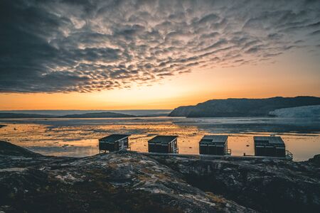 Greenland glacier nature landscape with famous Eqi glacier and lodge cabins. Midnight sun and pink...