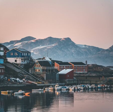 Sunset view of Maniitsoq arctic city in Greenland. Mountains in background during midnight sun. Colourfull houses and panorama. View to port with ships.の写真素材