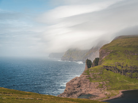 Faroe Islands Traelanipa the slaves rock cliff is seen rising over the ocean next to lake Sorvagsvatn. Clouds and blue sky during suommer on the island vagar in the Faroe Islands.の写真素材