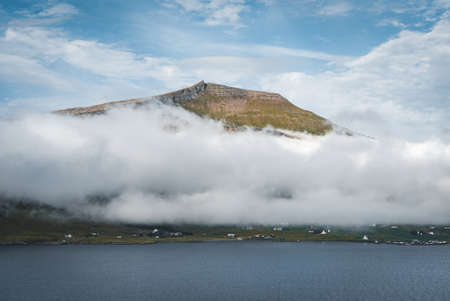 Spectacular views of clouds and fog covering the scenic fjords on the Faroe Islands on the island ov Vagar during a sunny day with blue sky.の写真素材