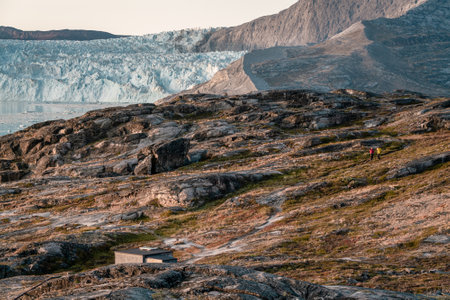 Unidentified People sitting standing in front of huge glacier wall of ice. Eqip Sermia Glacier Eqi...