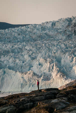Unidentified People sitting standing in front of huge glacier wall of ice. Eqip Sermia Glacier Eqi...