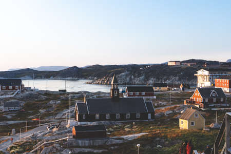 Aerial View of Arctic city of Ilulissat, Greenland during sunrise sunset with fog. Colorful houses in the center of the town with icebergs in the background in summer on a sunny day with orange pink sky. Photo taken in Greenland.の写真素材