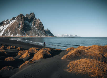 Young man tourist standing at beach during sunset runrise and gorgeous reflection of Vestrahorn mountain on Stokksnes cape in Iceland. Beautiful snow covered mountains. Location: Stokksnes cape, Vestrahorn Batman Mount , Iceland, Europe. Photo taken in Iceland.の写真素材