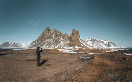 Young man traveler tourist standing in front of mountain Eystrahorn in east Iceland on a sunny winterday. Blue sky with snow covered mountain.の写真素材