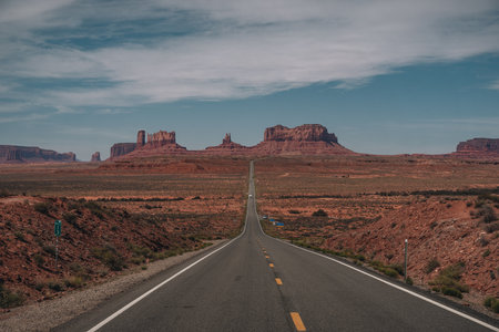 View of Monument Valley from Forrest Gump Point Mexican Hat, US-163 with street leading towards monuments. Blue sky and sunny day.の写真素材