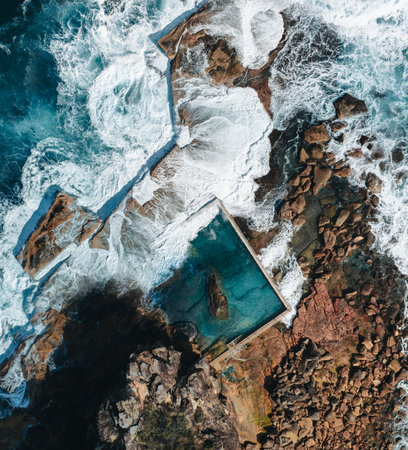 Aerial view early morning light with ocean waves flowing over rocks around North Curl Curl ocean rock pool during storm.の写真素材