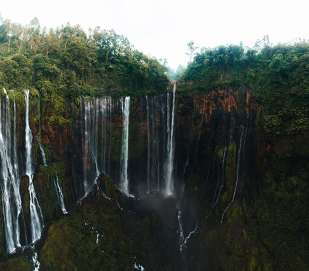 View from above, stunning aerial view of the Tumpak Sewu Waterfalls also known as Coban Sewu with the Semeru volcano in the distance, Malang Regency,East Java, Indonesia.の写真素材