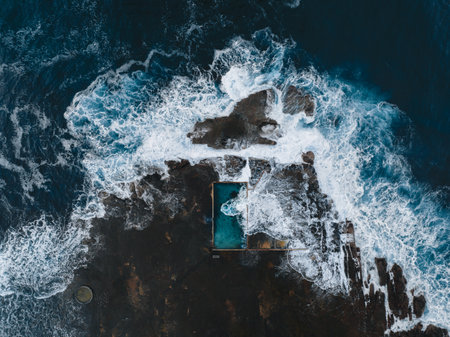 Aerial view early morning light with ocean waves flowing over rock pool. Ourie Pool, Gerringong. North Curl Curl ocean rock pool during storm. New South Wales, Australia.の写真素材