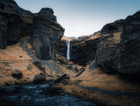 Kvernufoss waterfall in the gorge of the mountains. Tourist Attraction Iceland. Man in red jacket standing and looks at the flow of falling water. Beauty in natureの写真素材